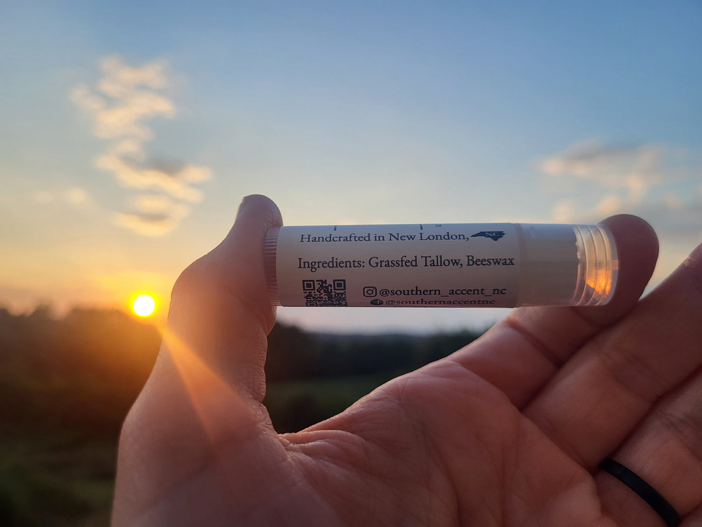 Hand holding a tube of tallow lip balm with sunset in the background