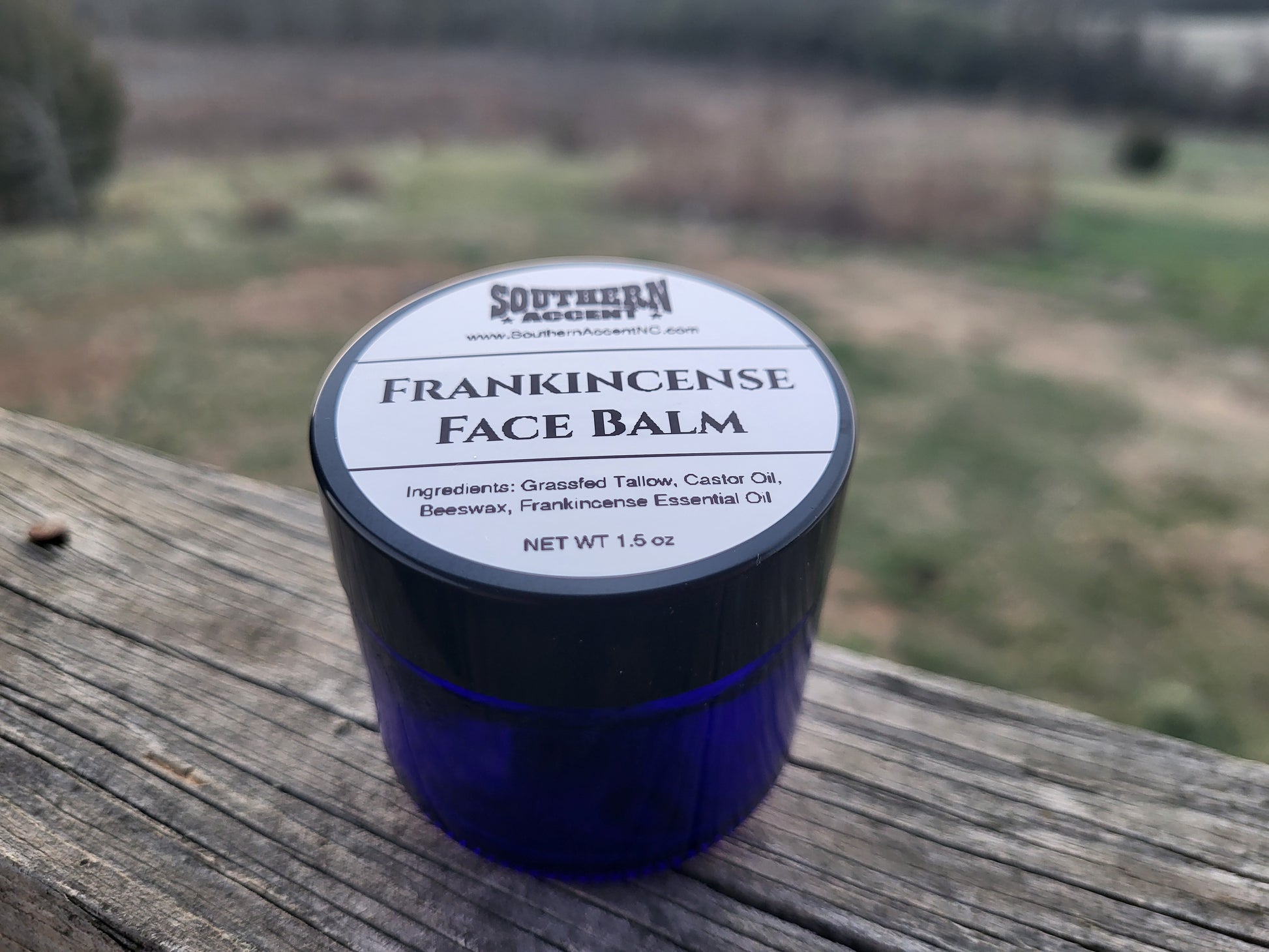 Blue jar of Southern Accent Frankincense Face Balm on a wooden surface with a blurred natural background at dusk