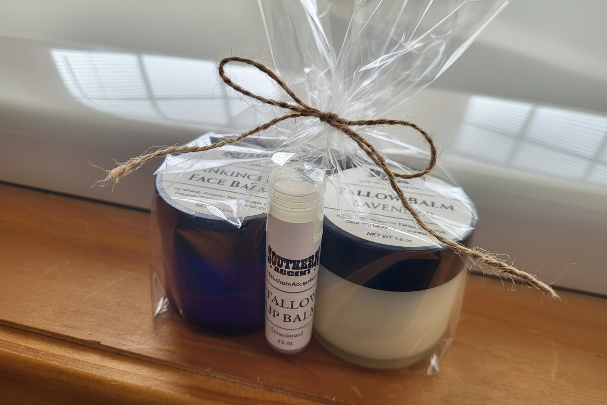 Premium tallow skincare ritual — The Tallow Essentials Set including two tallow balms and a lip balm wrapped in cellophane with jute twine on wood surface, bright natural light