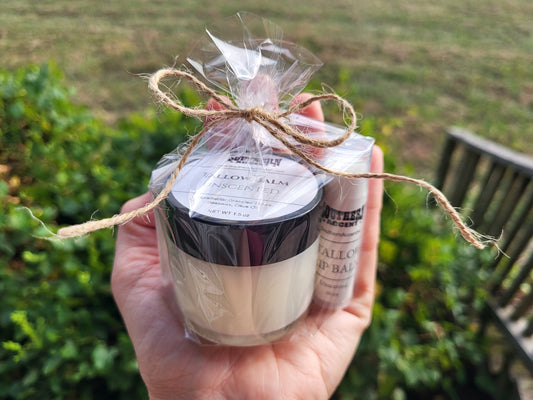 Hand holding a jar of southern accent tallow balm and lip balm wrapped in cellophane with twine, against a blurred natural background.